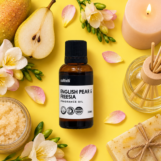 A bottle of cultini English Pear & Freesia fragrance oil is centered in a styled flat-lay on a bright yellow background, surrounded by a pear, flowers, a lit candle, a reed diffuser, bath salts, and a wrapped soap bar.