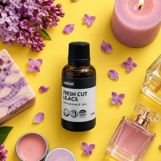 A bottle of Craftiviti Fresh Cut Lilacs fragrance oil is centered on a bright yellow background, surrounded by lavender flowers, a pink candle, a bar of soap, and perfume bottles, creating a cohesive scent-themed flat lay.