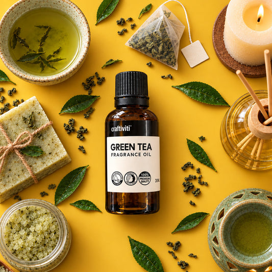 An amber glass bottle of craftiviti Green Tea Fragrance Oil is arranged in a styled flat-lay on a bright yellow background, surrounded by green tea leaves, a cup of green tea, a candle, a reed diffuser, and green tea soap and bath salts.