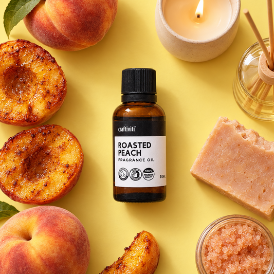 A bottle of cultivi' Roasted Peach Fragrance Oil is centered on a bright yellow background, surrounded by peach slices, a whole peach, a lit candle, a reed diffuser, a bar of soap, and a small jar of pink salt.
