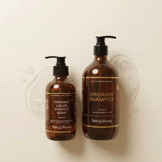 Two amber glass pump bottles of Yein&Young hair care products on a white background, with four circular certification badges on the right. The smaller bottle is Liquid Castile Soap, and the larger bottle is Organic Shampoo.