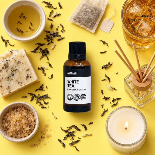 A close-up view of a white tea fragrance oil container with a background of loose tea leaves and a few pieces of fruit, suggesting the natural ingredients used in the product.