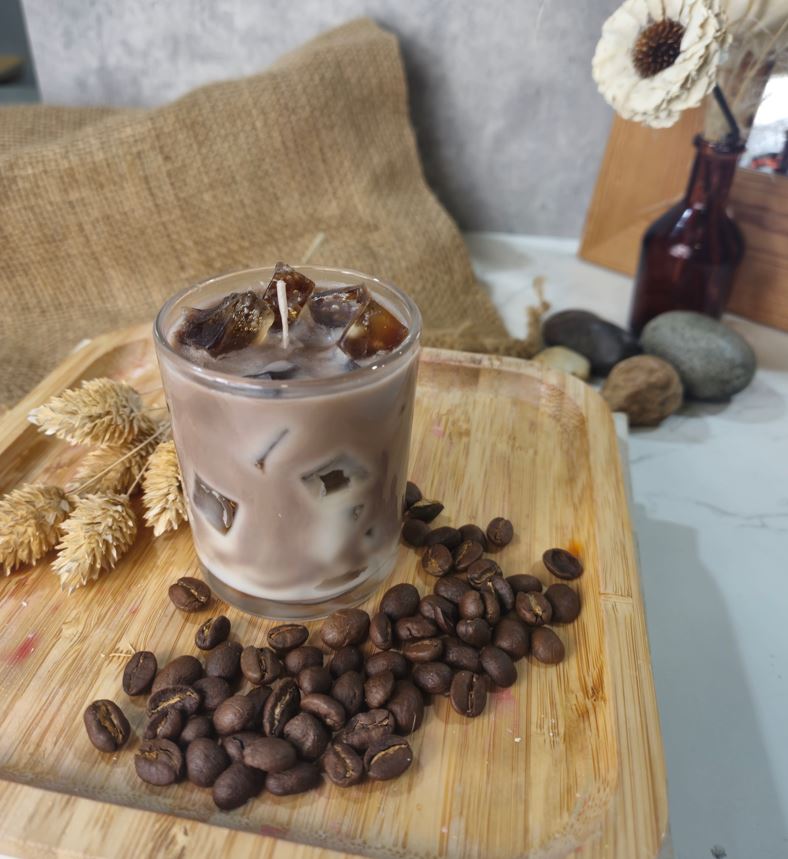 Candle in a glass with coffee beans on a wooden board, surrounded by coffee beans and decorative elements.